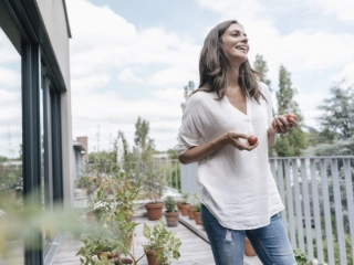 Frau steht auf ihrer Terrasse, schaut in die Ferne und hat kleine Tomaten in der Hand